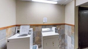 A laundry room with two washing machines and a dryer, a tiled wall, and a door. - Spiral-staircase Condo w/ Mountain-air Balcony (Girdwood)