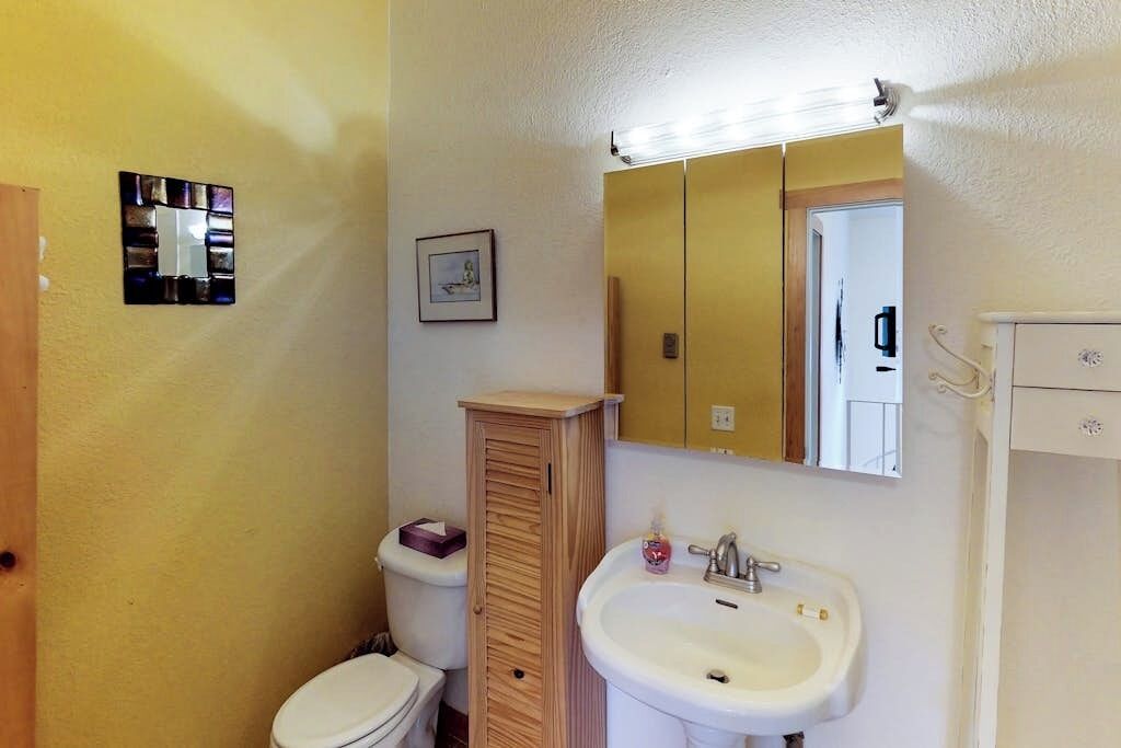 Et badeværelse med toilet, et træskab, en vask og et spejl.