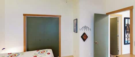Un dormitorio con cama, puerta, lámpara fijada a la pared y otra puerta con ventana.