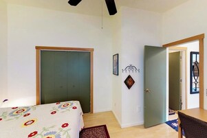 Un dormitorio con cama, puerta, lámpara fijada a la pared y otra puerta con ventana.