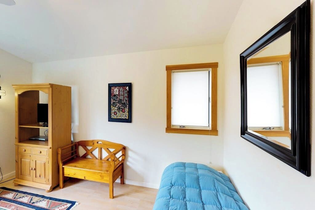 A room with a bed, a wooden cabinet, a bench, a framed picture, and two windows.