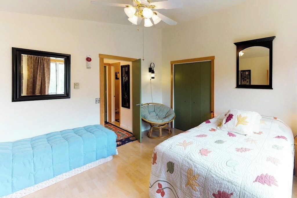 A bedroom with a bed, a chair, a wardrobe, a mirror, and a ceiling fan.