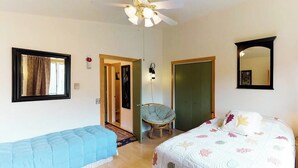 A bedroom with a bed, a chair, a wardrobe, a mirror, and a ceiling fan. - Spiral-staircase Condo w/ Mountain-air Balcony (Girdwood)