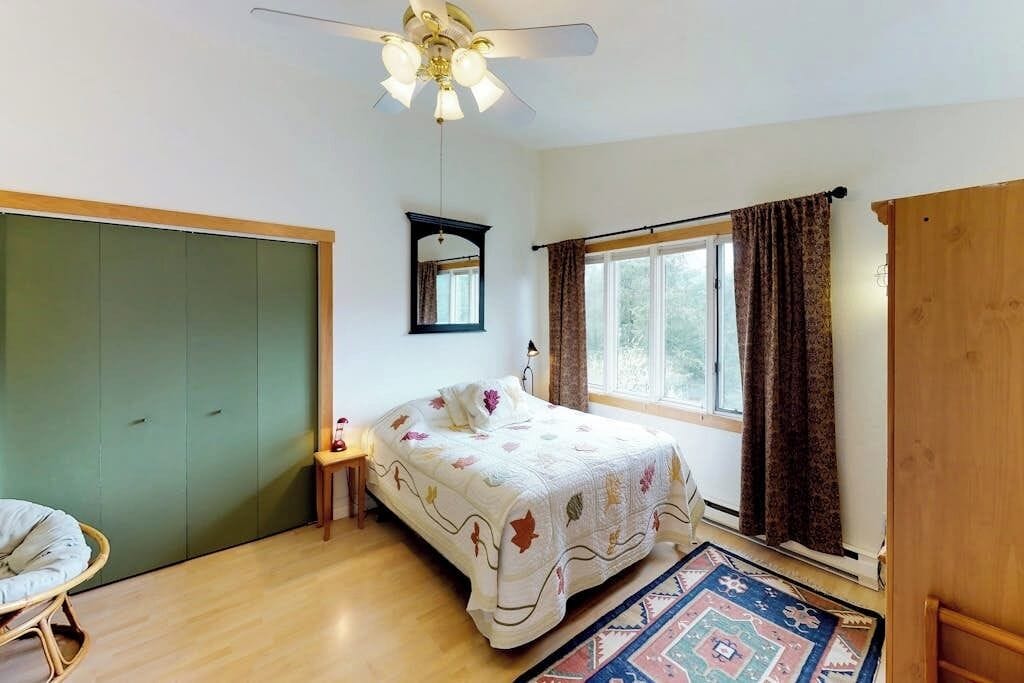 A bedroom with a bed, a window with curtains, a ceiling fan, and a green wardrobe.