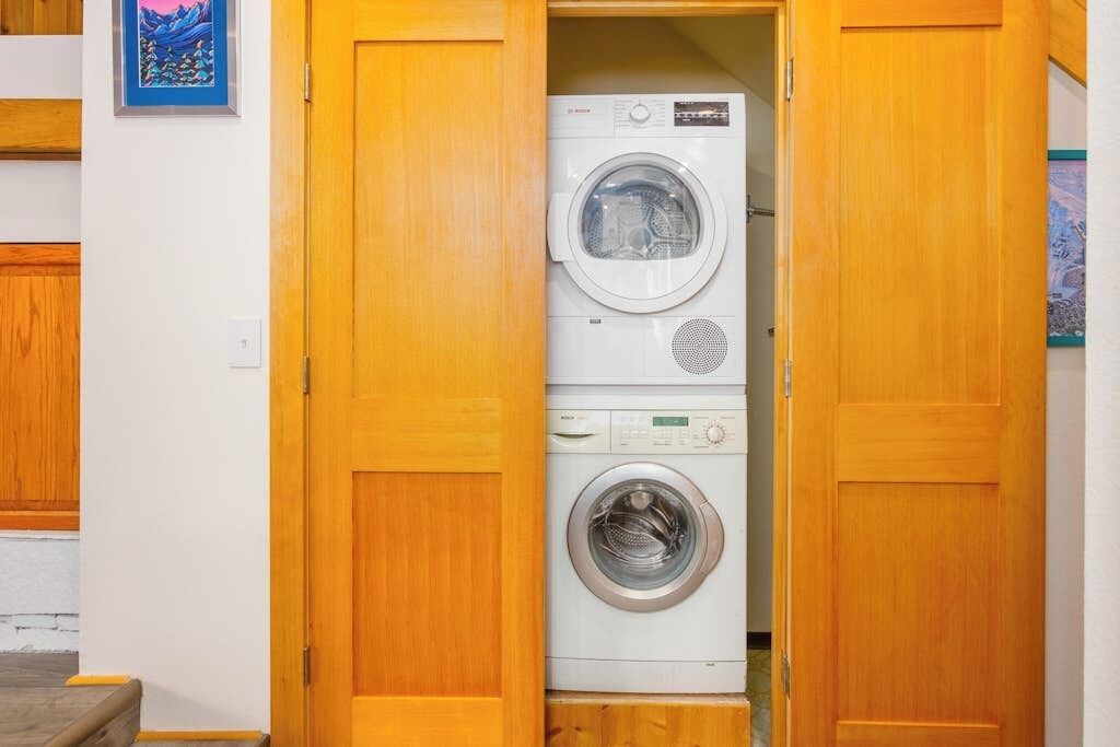 A laundry room with two stacked washing machines, wooden cabinets, and a framed picture on the wall.