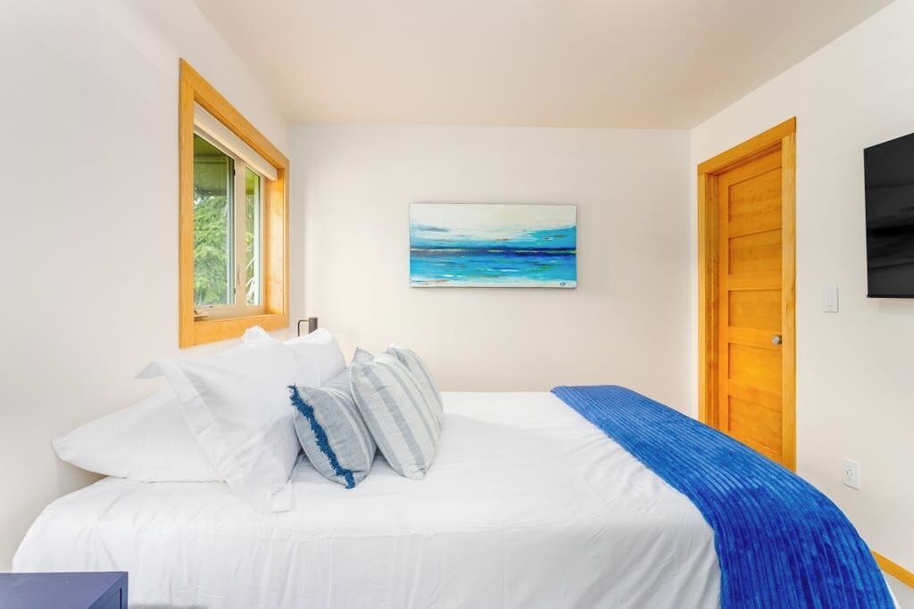A bedroom with a bed, a window, a painting, and a door.