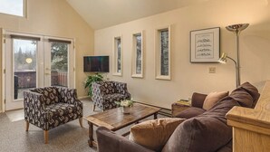 Ein Wohnzimmer mit einer Couch, zwei gemusterten Sesseln, einem Couchtisch, einem Fernseher und einem gerahmten Bild an der Wand.