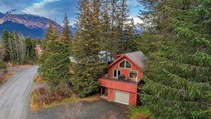 Eine rote Holzhütte mit Garage, umgeben von dichtem Wald und Bergen im Hintergrund.