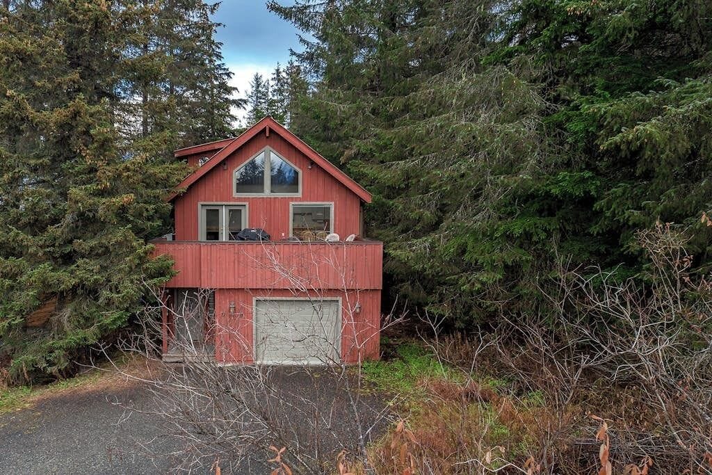 A red cabin with a garage, surrounded by dense forest.