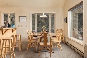 Un coin repas avec une table et des chaises en bois, un luminaire suspendu et une vue à travers une porte vitrée.