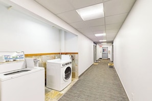 A hotel laundry room with a washing machine, dryer, and a carpeted floor.