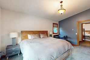 Una habitación de hotel con una cama grande, una mesita de noche con lámpara, un cabecero de madera y vista al mar a través de una ventana.