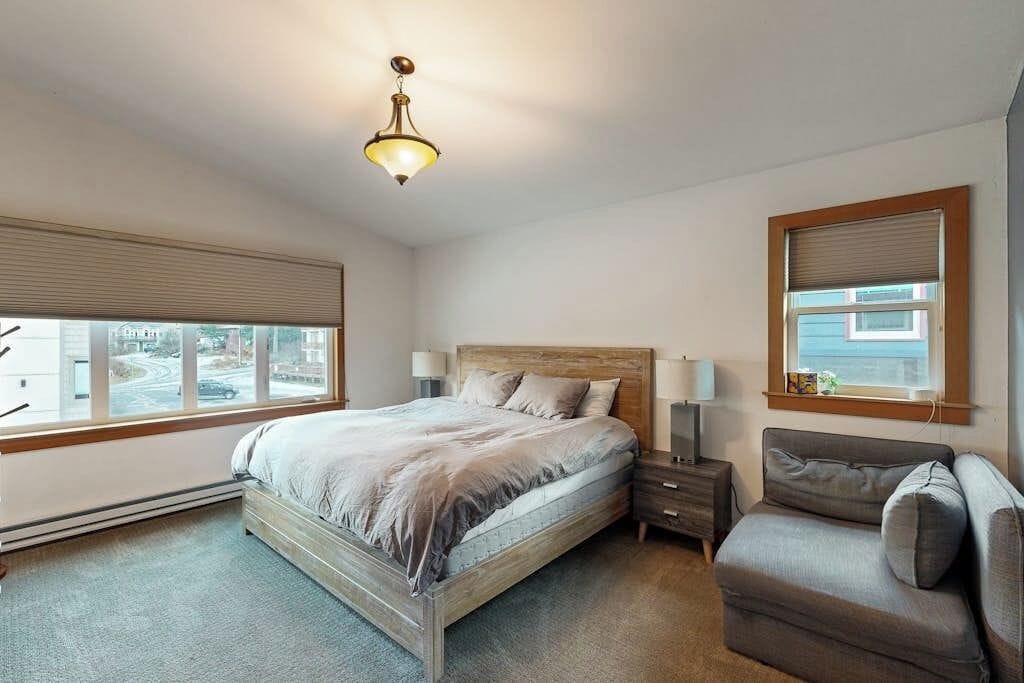 A bedroom with a bed, bedside tables, a nightstand, a sofa, a window with blinds, and a ceiling light fixture.