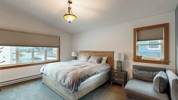 A bedroom with a bed, bedside tables, a nightstand, a sofa, a window with blinds, and a ceiling light fixture.