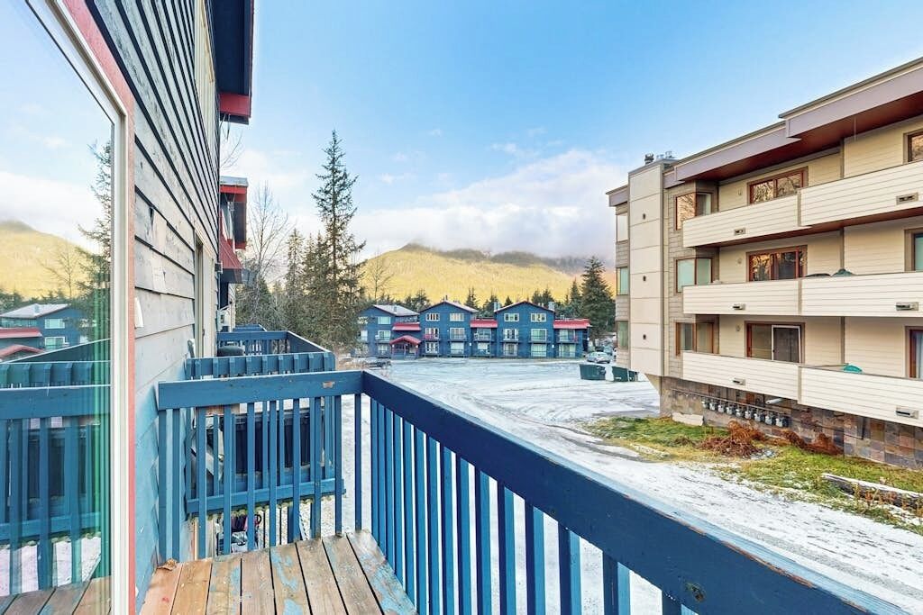 A multi-story building with a balcony, a view of a mountainous landscape, and a parking area.