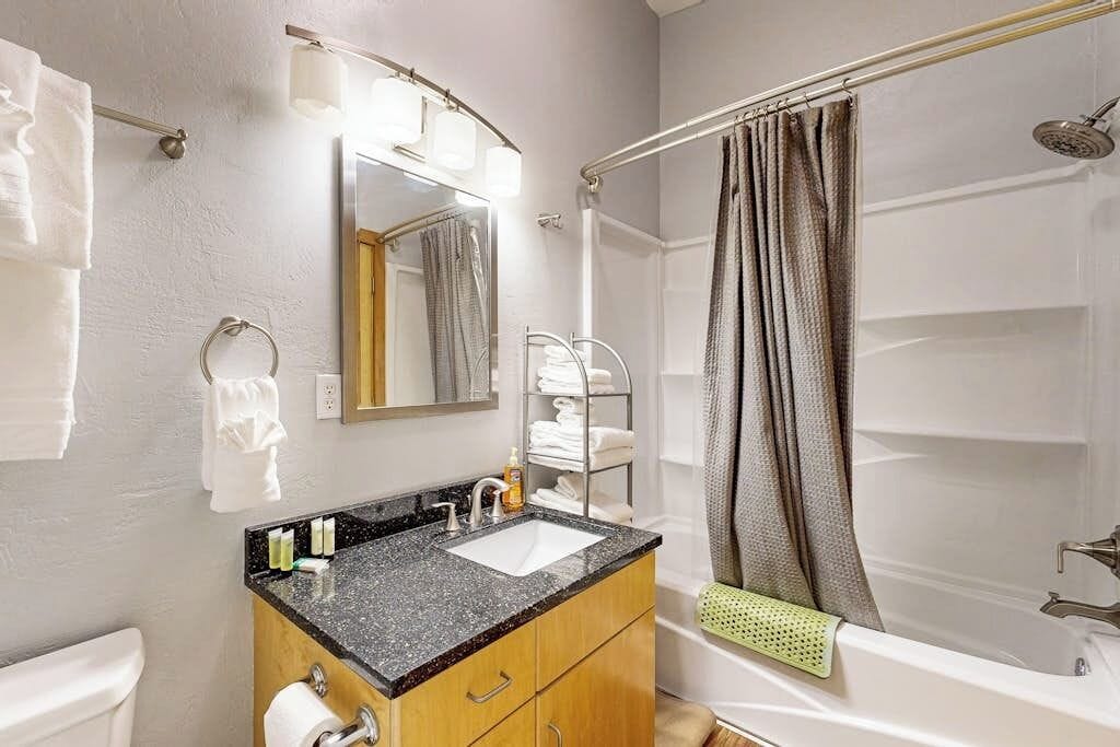 A bathroom with a sink, mirror, towel rack, shower curtain, and bathtub.