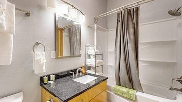 A bathroom with a sink, mirror, towel rack, shower curtain, and bathtub.