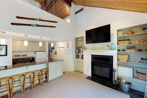 A modern kitchen with a fireplace, bar stools, and a TV mounted above the fireplace.