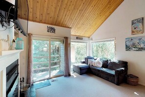 A modern living room with a fireplace, a large window, and a ceiling with wooden beams.