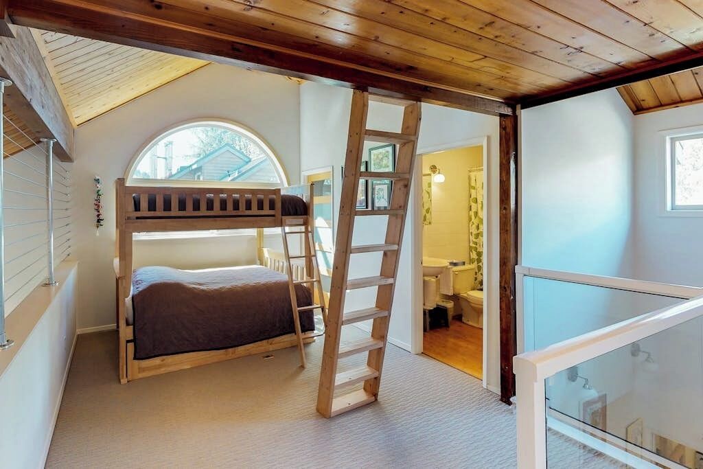 A room with a bunk bed, a wooden ladder, a skylight, and a view of the outside.