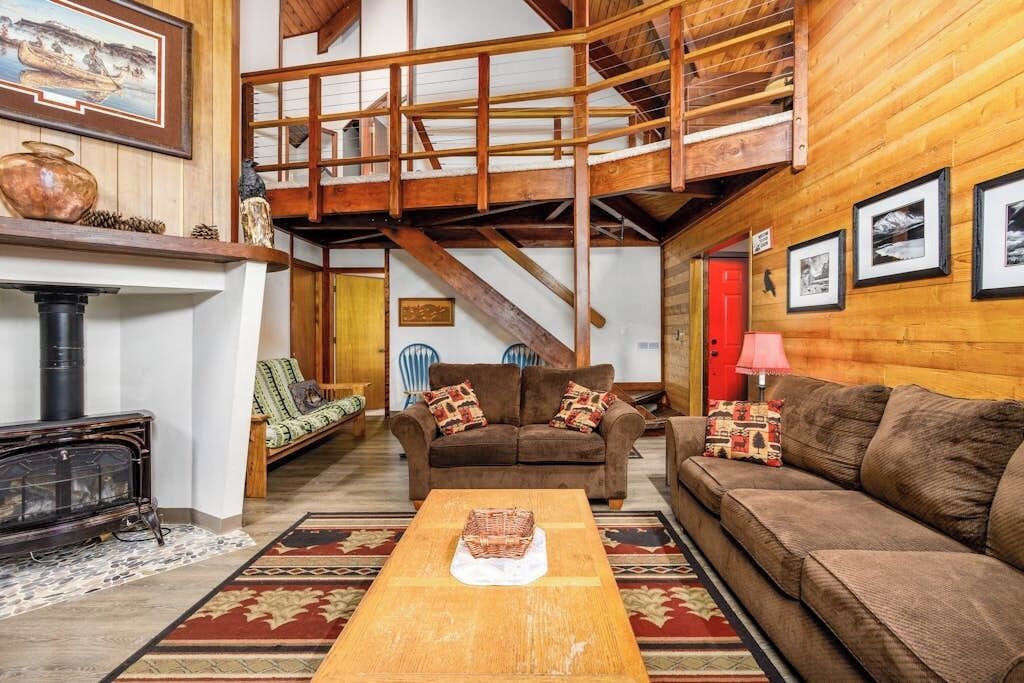 A cozy living room with a fireplace, a wooden staircase, and a high ceiling.