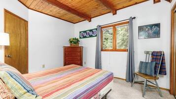 A bedroom with a bed, a dresser, a window with curtains, a chair, and a wall decoration.