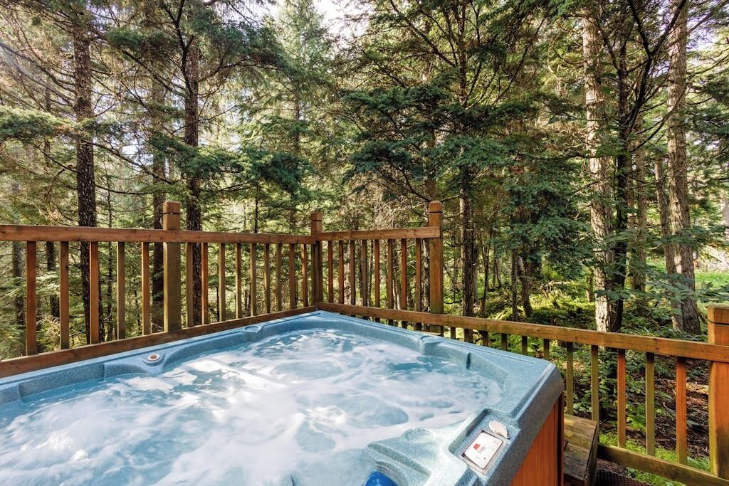 A hot tub surrounded by a wooden deck and dense forest.
