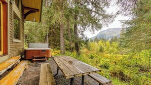 Una mesa de picnic de madera con bancos, un jacuzzi y una casa con porche.