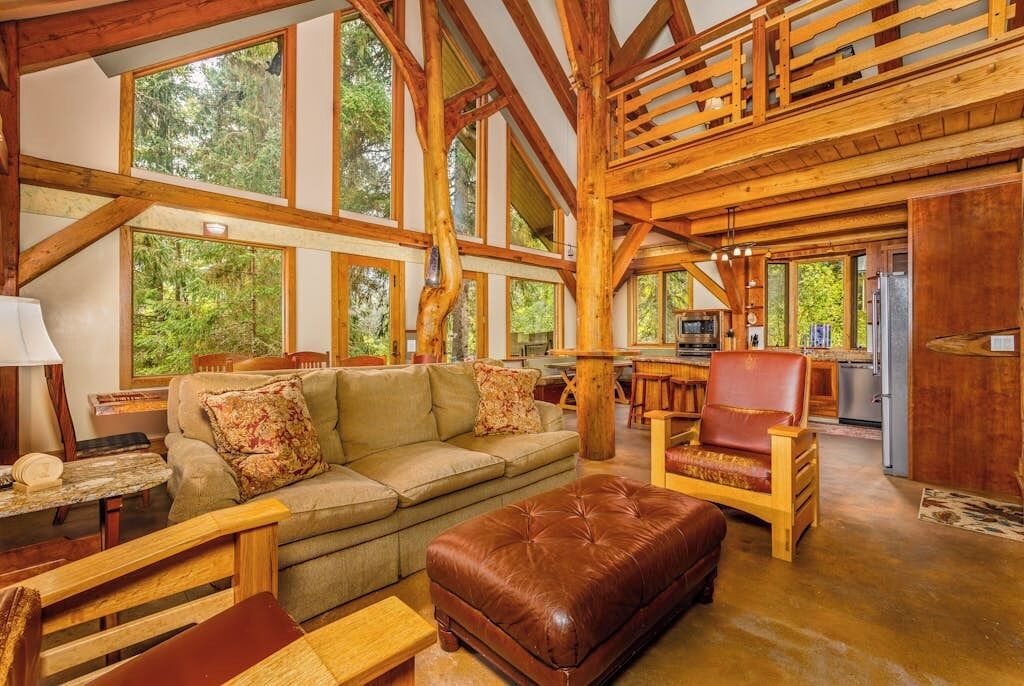 A spacious living area with a high ceiling, wooden beams, and large windows offering a view of the outdoors.