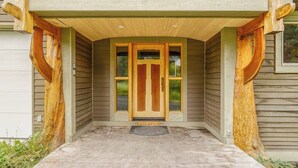 Una puerta principal de madera con un panel de vidrio, un porche de concreto y un felpudo de metal.