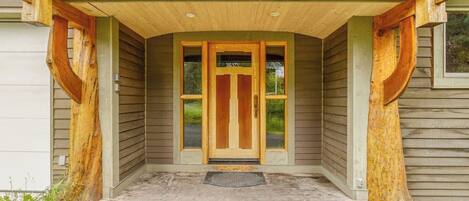 A wooden front door with a glass panel, a concrete porch, and a metal doormat.