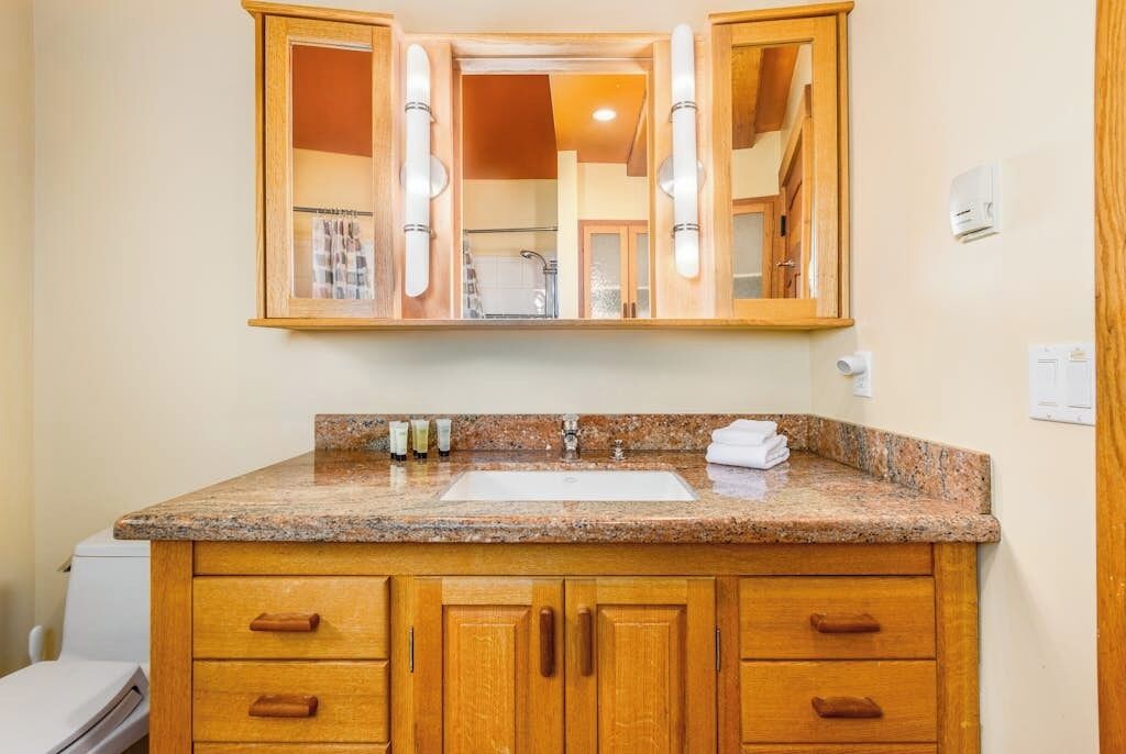 A bathroom with a granite countertop, wooden cabinets, a white sink, and a mirror above the sink.