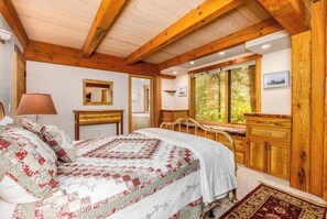 Ein Schlafzimmer mit einem großen Bett, Holzbalkendecke, einem Fenster mit Blick ins Grüne und einer Holzkammer.
