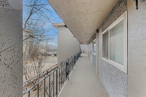 A covered corridor with a metal railing, a concrete floor, and a building facade with windows. - Practical Anchorage Apartment Built for Families (Anchorage)