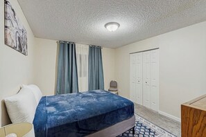 A bedroom with a bed, a chair, a wardrobe, and a ceiling light. - Practical Anchorage Apartment Built for Families (Anchorage)