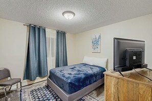 A bedroom with a bed, a desk, a chair, a television, and a window with curtains. - Practical Anchorage Apartment Built for Families (Anchorage)
