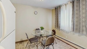 A dining area with a round glass table, four chairs, a clock on the wall, and patterned curtains. - Practical Anchorage Apartment Built for Families (Anchorage)