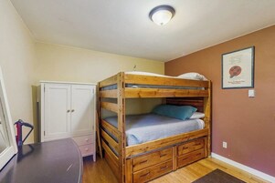 Una cama litera con cabecera, un armario blanco y un cuadro en la pared.
