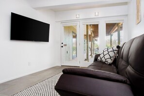 A living room with a flat-screen TV mounted on the wall, a brown leather sofa, and a patterned rug.