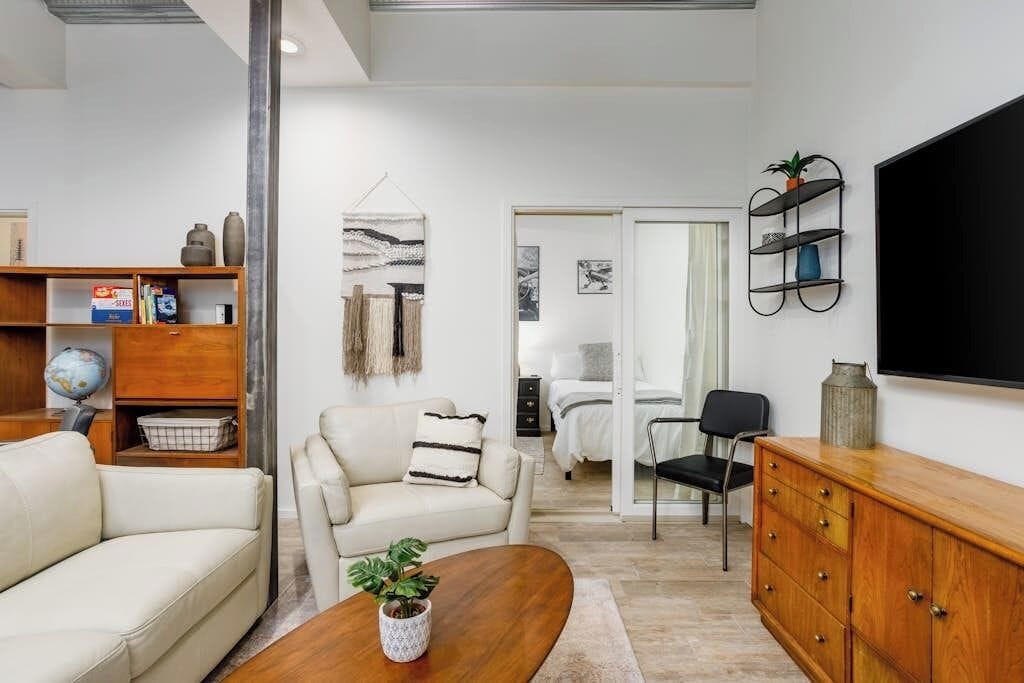 Un salon moderne comprenant un canapé, un fauteuil, une table basse et un téléviseur fixé au mur.