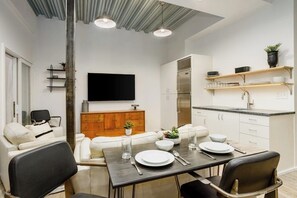A modern kitchen with white cabinets, a stainless steel refrigerator, and a dining area with a table set for two.