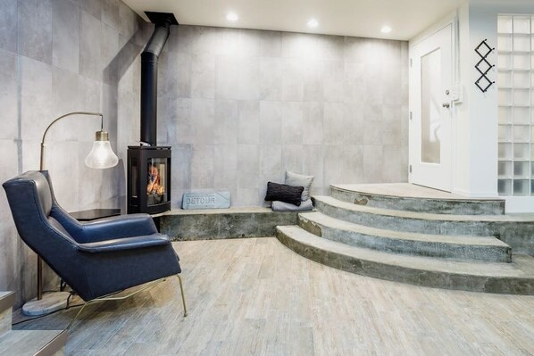 A modern interior with a stone wall, a fireplace, a blue chair, and a staircase leading to a door.