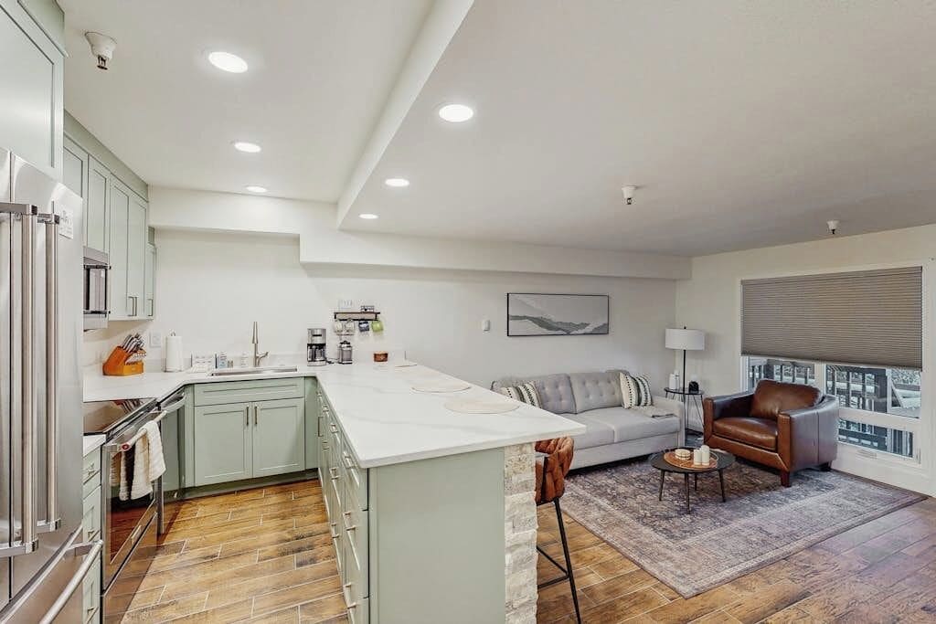 Una cocina moderna con una isla central, una zona de comedor con sofá y sillas, y un amplio ventanal con persianas.