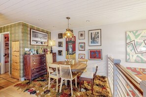 A dining area with a wooden table and chairs, a chandelier, and artwork on the walls. - One-bedroom Loft in Anchorage's Bootlegger Cove (Anchorage)