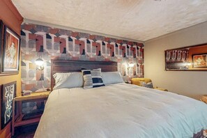 A hotel room with a large bed, a patterned headboard, wall-mounted lamps, and artwork. - One-bedroom Loft in Anchorage's Bootlegger Cove (Anchorage)