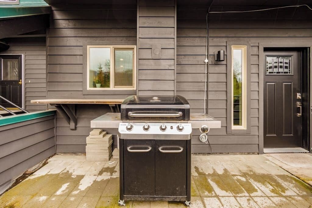 Una parrilla para barbacoa y una estufa portátil instaladas afuera de una casa con ventana y puerta.