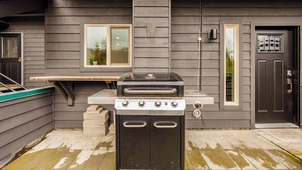 Una parrilla para barbacoa y una estufa portátil instaladas afuera de una casa con ventana y puerta.