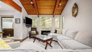 Una sala de estar con techo de madera, una chimenea, un sofá, una mesa de centro y un televisor.