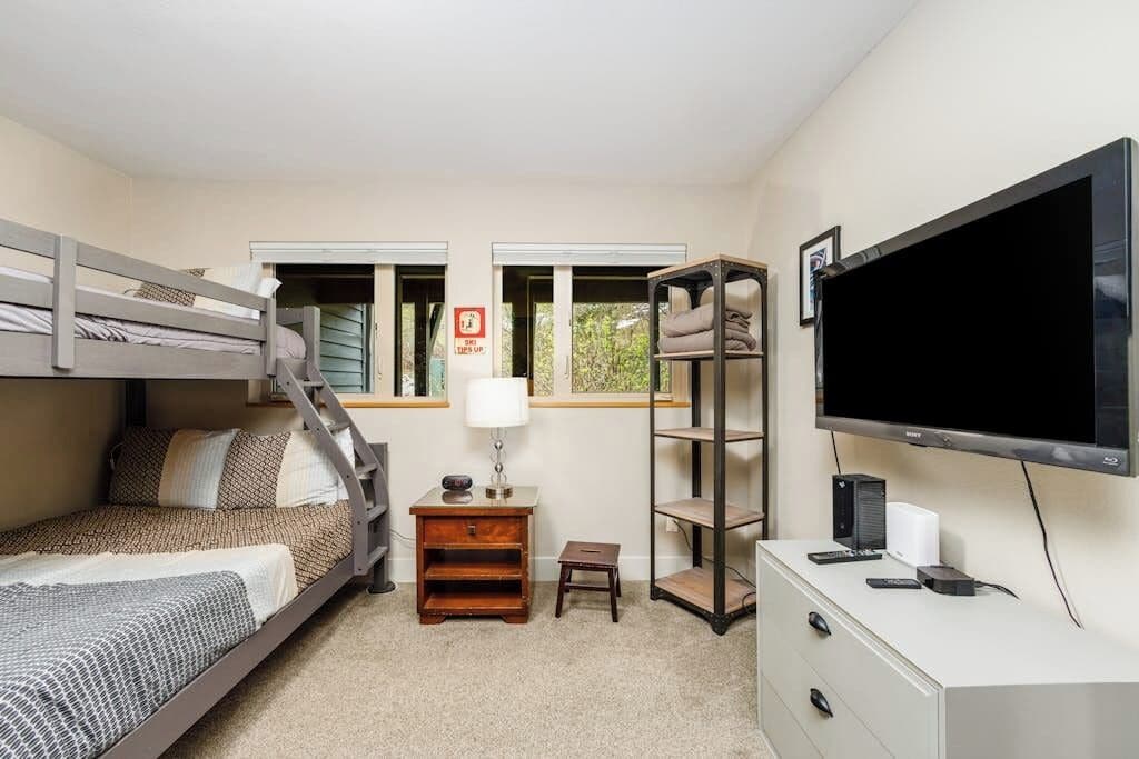 A bedroom with bunk beds, a desk, a TV, and a shelf.