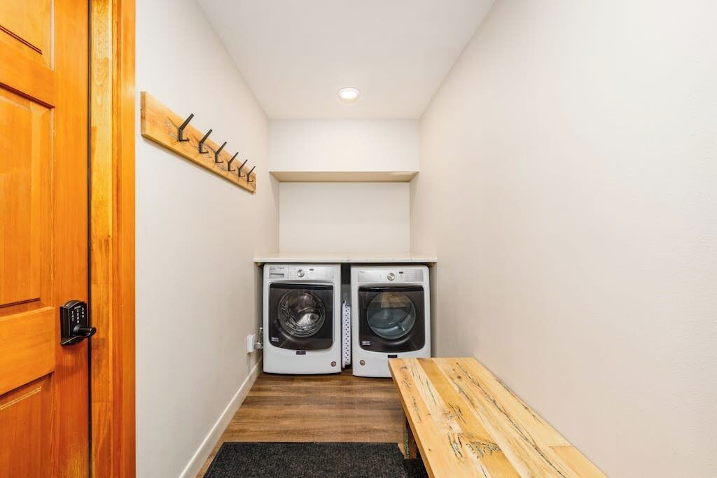 A laundry room with two washing machines, a wooden bench, and a coat rack.
